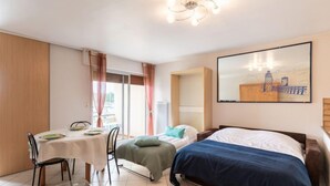 Een hotelkamer met een bed, een eettafel met stoelen, een klein tafeltje met een glazen blad en een schilderij aan de muur.