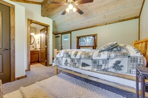Ein Schlafzimmer mit Holzboden, einem Bett mit kariertem Überwurf, einem Holz-Kopfteil und einem Deckenventilator.