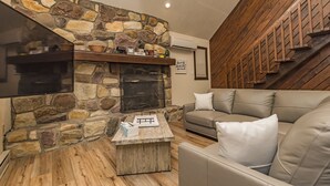 Ein gemütliches Wohnzimmer mit Kamin aus Stein, einer Holztreppe und einem Ledersofa.