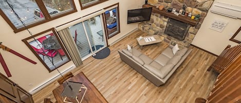 A spacious living area with a stone fireplace, a large window overlooking a deck, and a cozy seating arrangement.