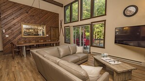 Ein modernes Wohnzimmer mit einem großen Ledersofa, einem Holzesstisch und einem an der Wand befestigten Fernseher.