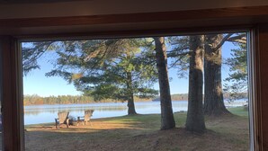 A view from a window overlooking a lake with two Adirondack chairs on the shore. - Peaceful Lakefront Home for Rent on Side Lake chain of lakes! (Side Lake)