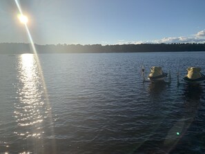 A calm lake with a clear sky, two boats anchored near the shore, and a forested hill in the background.