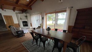 A dining area with a wooden table and chairs, a fireplace, and a view of a lake. - Peaceful Lakefront Home for Rent on Side Lake chain of lakes! (Side Lake)