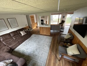 A cozy living room with a brown leather sofa, a grey rug, wooden flooring, a TV mounted on the wall, and a wooden cabinet.