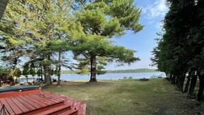 A deck with steps leading to a grassy area by a lake, surrounded by trees. - Peaceful Lakefront Home for Rent on Side Lake chain of lakes! (Side Lake)