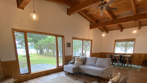 A spacious living room with a wooden ceiling, large windows, a sofa, and a coffee table. - Peaceful Lakefront Home for Rent on Side Lake chain of lakes! (Side Lake)