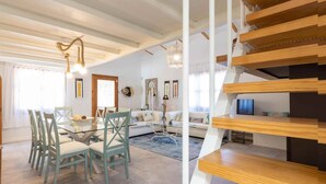 Una sala de estar moderna con una mesa de comedor de vidrio, sillas color esmeralda, un sofá blanco y una escalera de madera.