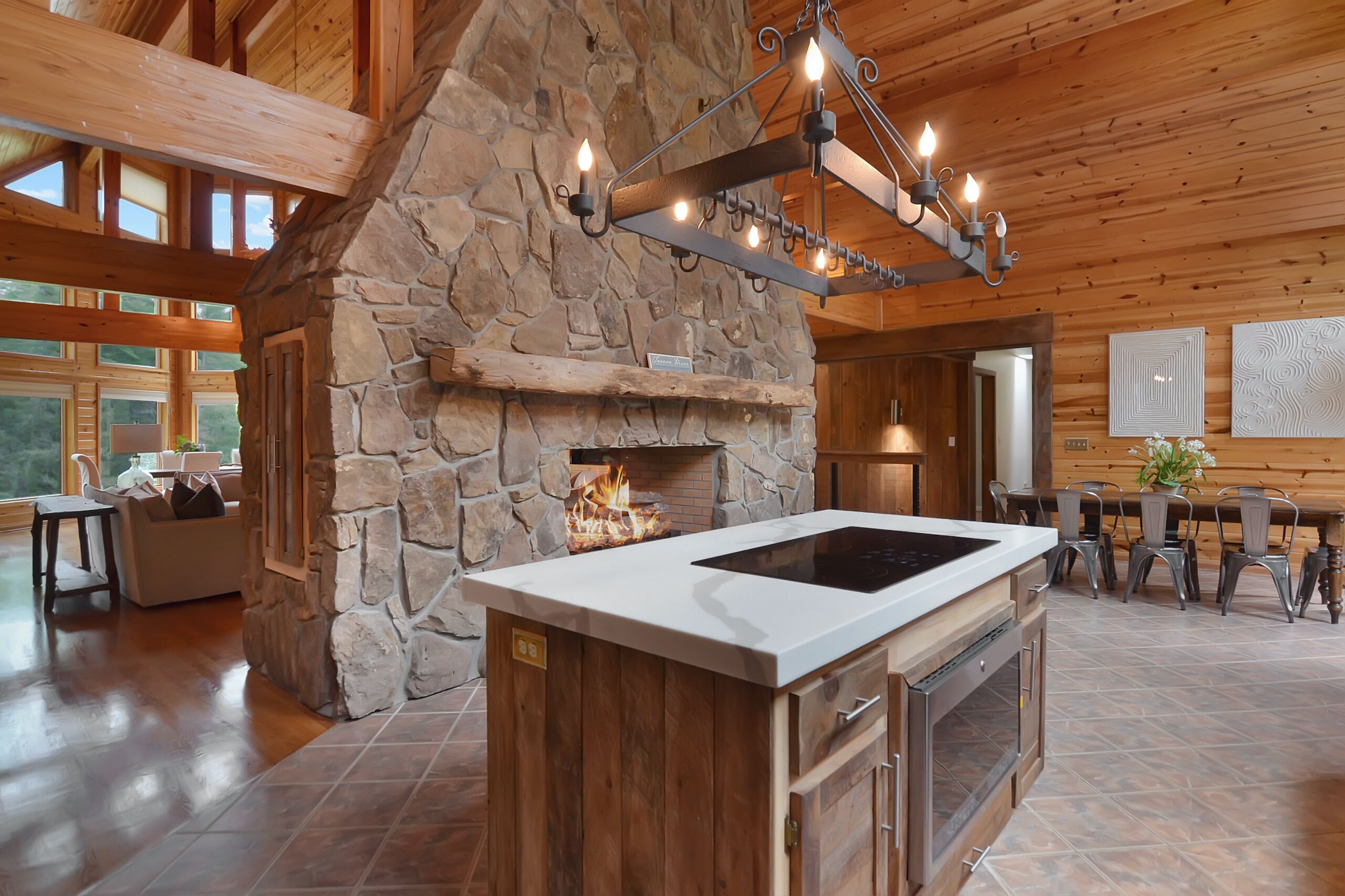 A spacious kitchen with a stone fireplace, wooden beams, and a modern island.