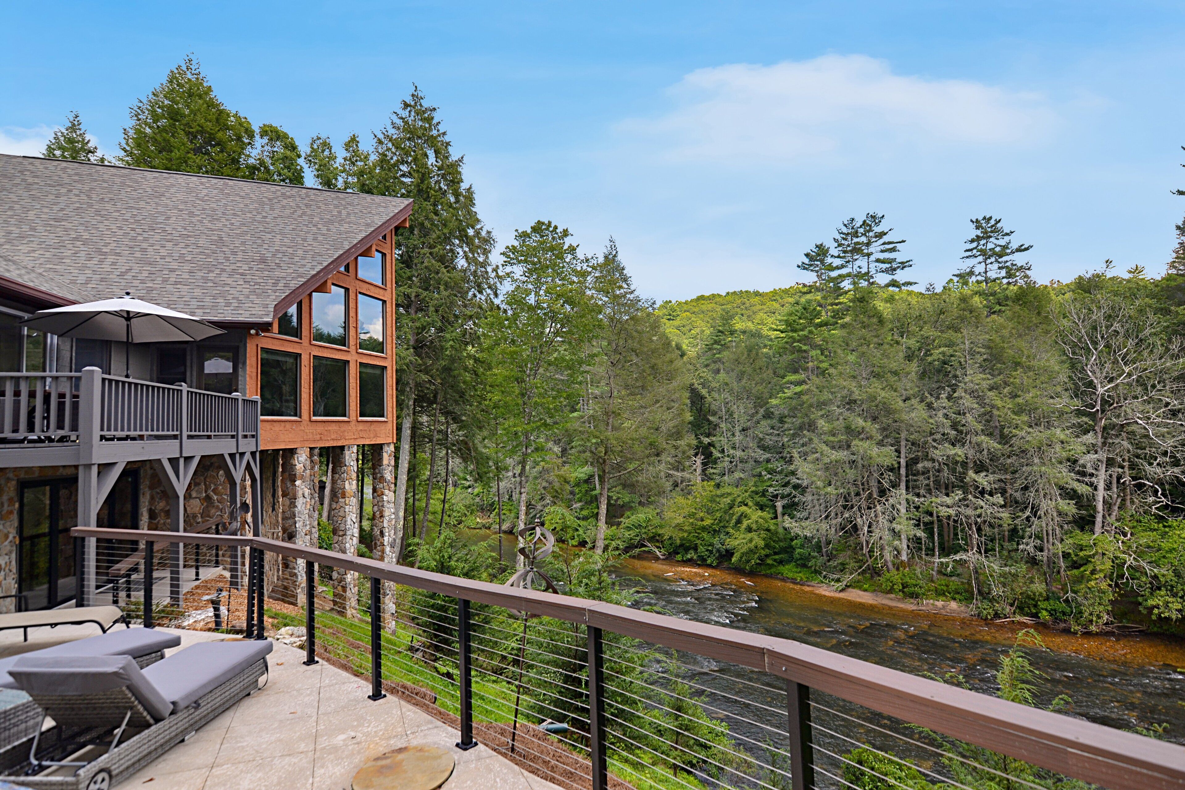 A two-story building with a balcony overlooking a river, surrounded by forest.