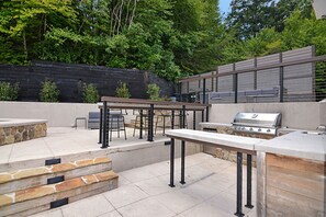 An outdoor patio with a grill, seating, and steps leading to a stone wall. - Toccoa Riverside Retreat ~ 45-Acre Estate, Fire Pit, Pool, Sauna, & More! (Blue Ridge)