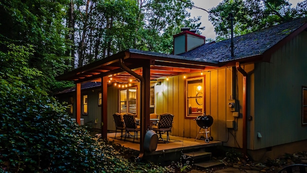 A cozy outdoor patio with a covered seating area, a grill, and a stone pathway leading to the house. - Stylish and Cozy Retreat in Gatlinburg-Family and Pet Friendly-Quaint and Quiet (Gatlinburg)