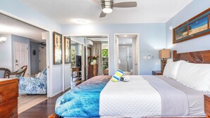 A bedroom with a large bed, a ceiling fan, and a painting on the wall. - Maui Banyan G202 - King Bed, Ocean View, Across from Kamaole Beach (Kihei)