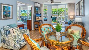 A living room with a sofa, wicker chairs, a glass coffee table, and a TV. - Maui Banyan G202 - King Bed, Ocean View, Across from Kamaole Beach (Kihei)