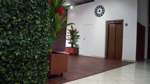 A hallway with a wooden floor, a clock on the wall, a potted plant, and an elevator. - Family Apt with Fast internet near park Carolina (Quito)
