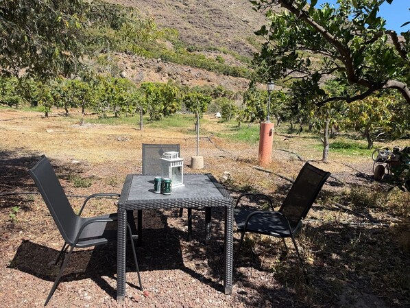 An outdoor table with two chairs, a lantern, and two cans on a gravel surface.