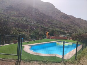 Une piscine entourée d’une clôture, une pelouse et un paysage montagneux en arrière-plan.