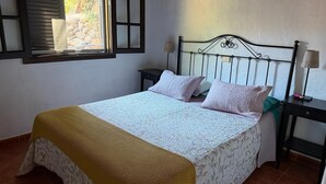 A bedroom with a bed, two bedside tables, a window with blinds, and a lamp. - Country Cabin "Finca Nim 2" on a Farm with Mountain View, Pool & Wi-Fi (Mogán)