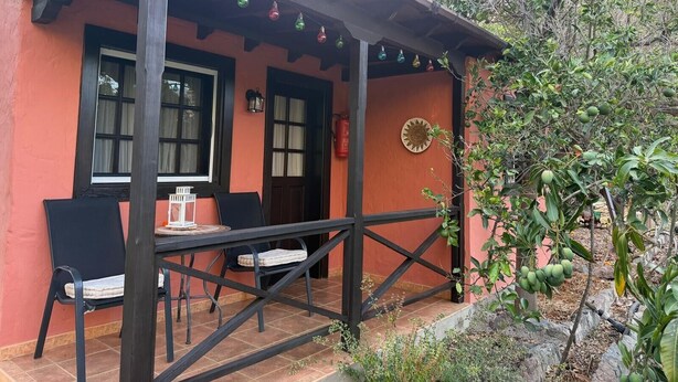 Un espace extérieur abrité, avec une table et des chaises, une pergola en bois et une lanterne fixée au mur.
