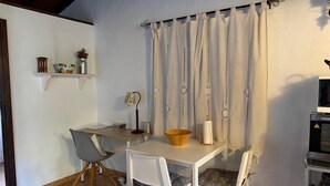 Un coin repas avec une table et des chaises, une petite étagère avec des objets décoratifs, une lampe et un téléviseur.
