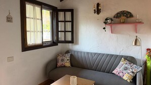 Une pièce chaleureuse avec un canapé gris, une petite table en bois, une fenêtre avec des rideaux, des étagères fixées au mur et une lampe fixée au mur.