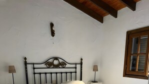 Un lit simple avec une couvre-lit blanche, dans une pièce dont le sol est carrelé et dont le plafond est orné de poutres en bois.