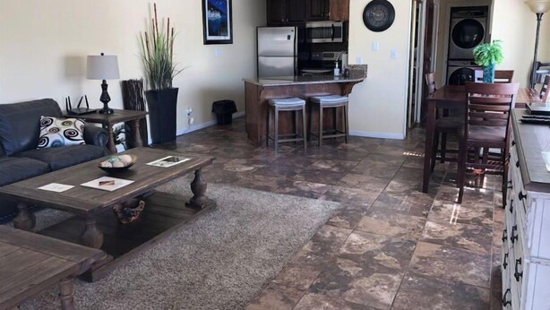 Una sala de estar con sofá, mesa de centro y una cocina equipada con refrigerador, microondas y taburetes de bar.