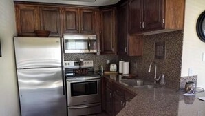 Una cocina con armarios de madera, electrodomésticos de acero inoxidable, encimera de granito y salpicadero azulejado.