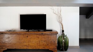 Un mueble de madera con un televisor encima, un jarrón verde con ramas y una pared blanca.