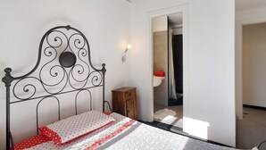Un dormitorio con estructura de cama metálica, una mesita de noche y un baño visible a través de una puerta abierta.