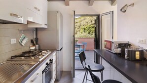 Una cocina moderna con estufa a gas, horno y microondas, que da a un balcón con vistas a zonas verdes.