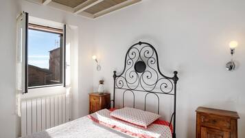 Una camera da letto con un letto, una finestra, un termosifone, un mobiletto in legno e luci a parete.
