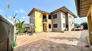 A two-story residential building with a basketball hoop, a gated entrance, and a paved driveway. - Hidden Gem In Oyibi New 2 Luxury Bedroom Apartment (Oyibi)