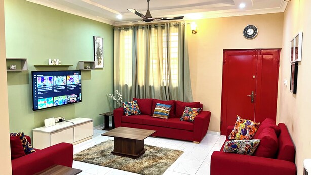 A living room with a red sofa, a coffee table, a TV, and a red door. - Hidden Gem In Oyibi New 2 Luxury Bedroom Apartment (Oyibi)