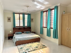 A bedroom with a bed, nightstands, a wooden wardrobe, and a ceiling fan. - Hidden Gem In Oyibi New 2 Luxury Bedroom Apartment (Oyibi)