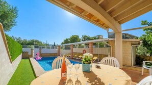 Un patio con una mesa lista para dos personas, una piscina y una cerca blanca.