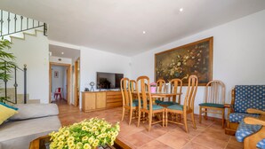 A living room with a sofa, dining table, chairs, a TV, and a painting on the wall.