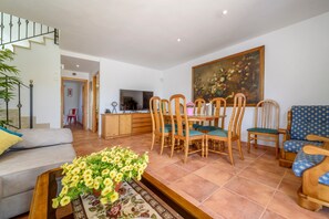 Un salon comprenant un canapé, une table à manger, des chaises, un téléviseur et un tableau accroché au mur.