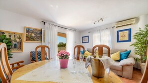 A dining area with a wooden table, chairs, a pink flower pot, and a sofa with cushions.