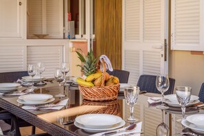 A dining table set with plates, cutlery, and a fruit basket. - Chalet Estrella de mar verde with Pool, A/C, Wi-Fi, Garden, Terrace & Balcony (puerto de alcudia)