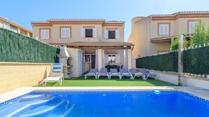 A swimming pool with lounge chairs, a covered patio, and a building with multiple windows and shutters.