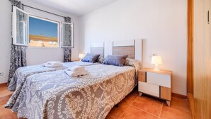 A double bed with patterned bedding, a bedside table with a lamp, and a window with curtains.