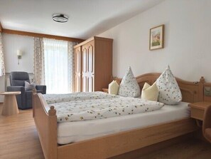 A bedroom with a wooden bed, a chair, a desk, and a wardrobe.