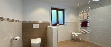 A modern bathroom with a toilet, bidet, and a small stool.