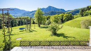 A garden with a wooden swing set, a small tree, and a view of mountains. - Vacation apartment Zuhaus- 2 persons, 45sqm, terrace with mountain view (Bad Reichenhall)