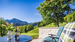 A patio with a round table, chairs, a vase with flowers, and a bottle of wine. - Vacation apartment Zuhaus- 2 persons, 45sqm, terrace with mountain view (Bad Reichenhall)