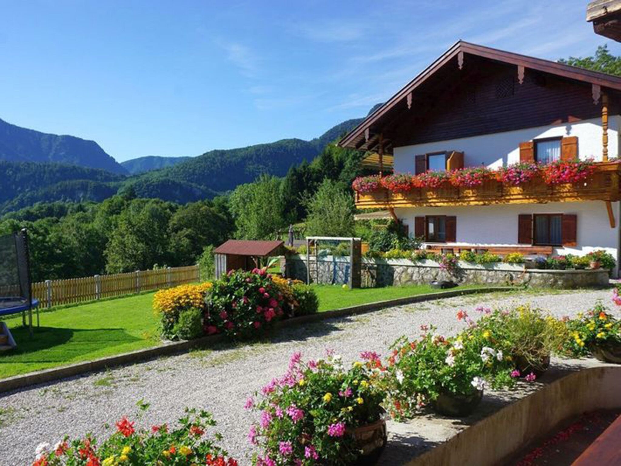 A traditional chalet with a balcony adorned with flowers, surrounded by a well-maintained garden and a view of mountains.