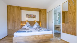 A modern bedroom with a wooden bed frame, a headboard with a built-in shelf, and a large mirror on the wall. - Vacation apartment in the farmhouse- 2 persons, 30sqm, balcony with mountain view (Bad Reichenhall)