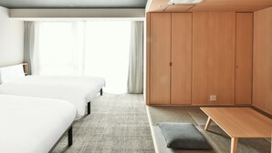 Quarto de hotel com duas camas, um guarda-roupa, um banco e uma janela com cortinas.