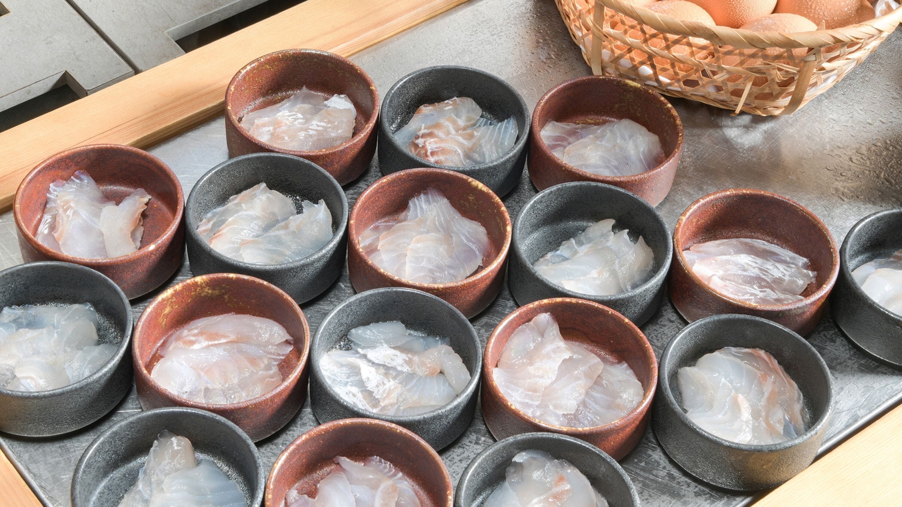 A display of raw fish in small ceramic bowls on a metal tray.